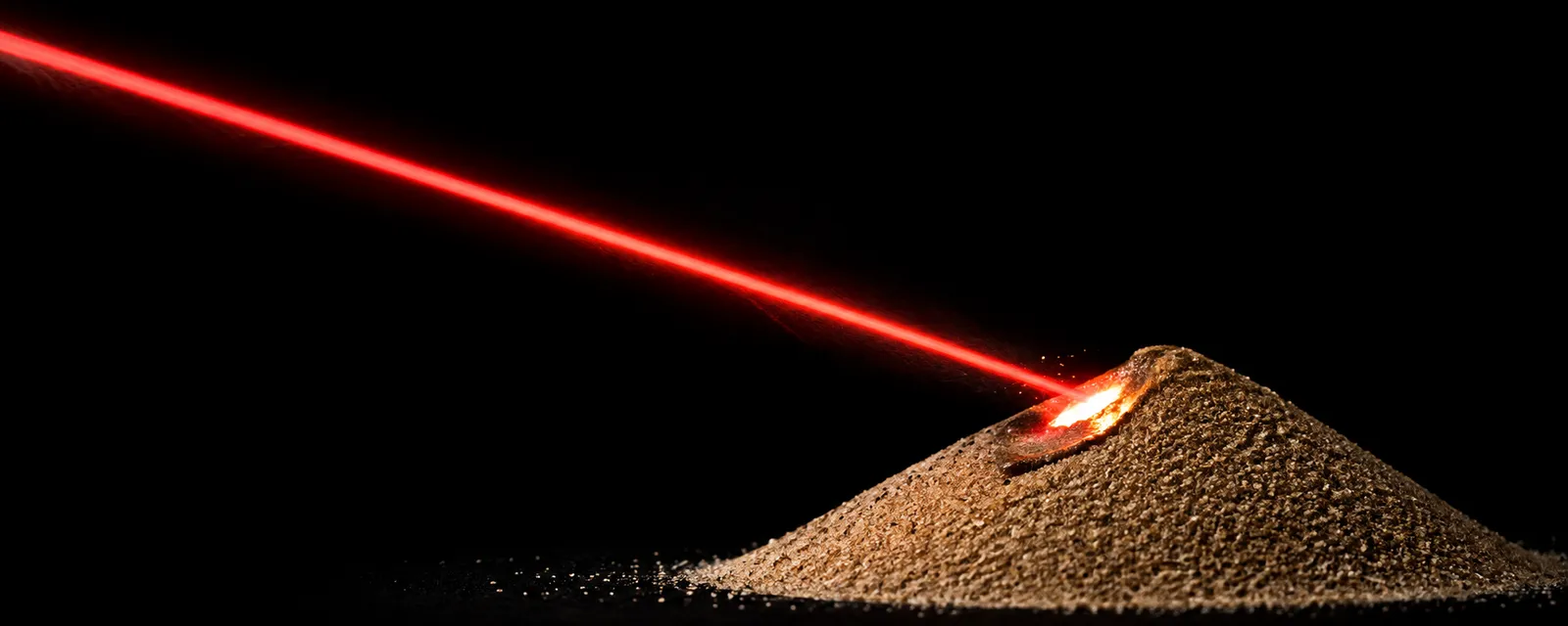 A red laser beam striking a mound of sand, melting its peak into glowing molten glass against a black background.